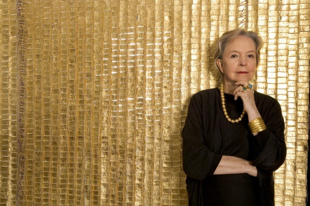 Woman standing in front of a gold-leaf, hanging textile.